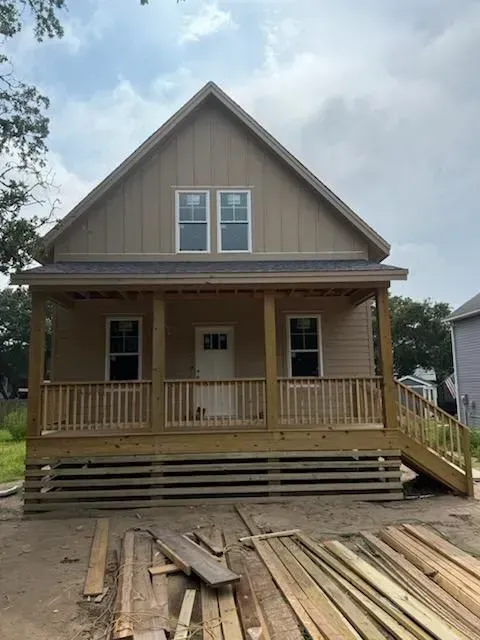Front view of a tan house under construction with a porch, stairs, and lumber stacked in front