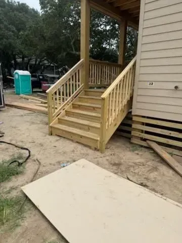 Wooden accessibility ramp and stairs leading to a house porch, with a plywood sheet on the ground.