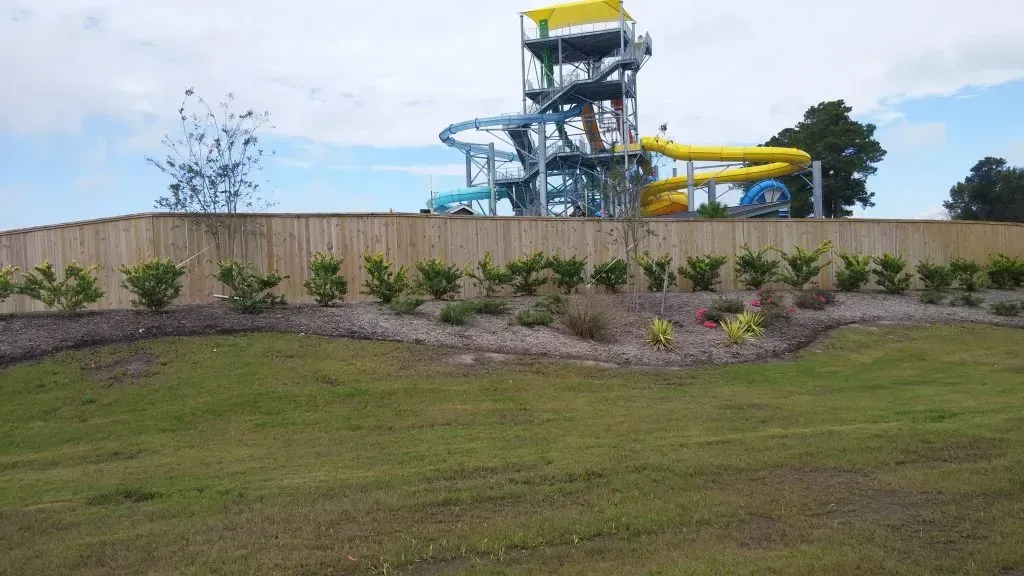 Water slides behind a beige wall above a landscaped grassy slope and shrubs