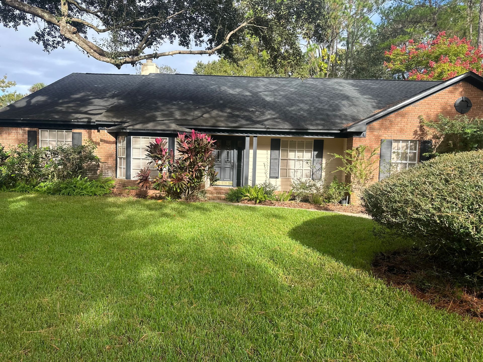 Tan house with black roof, green lawn, and shrubbery.