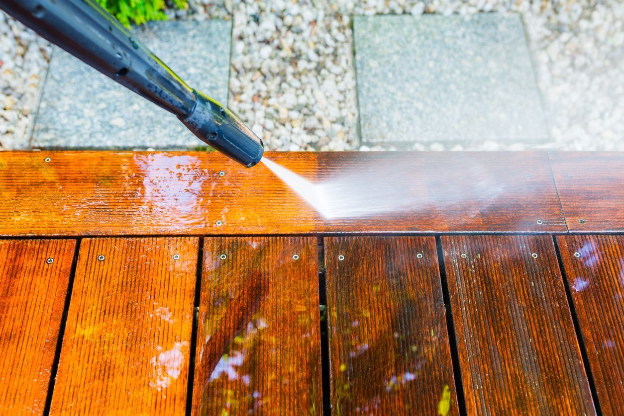A person is using a high pressure washer to clean a wooden deck.