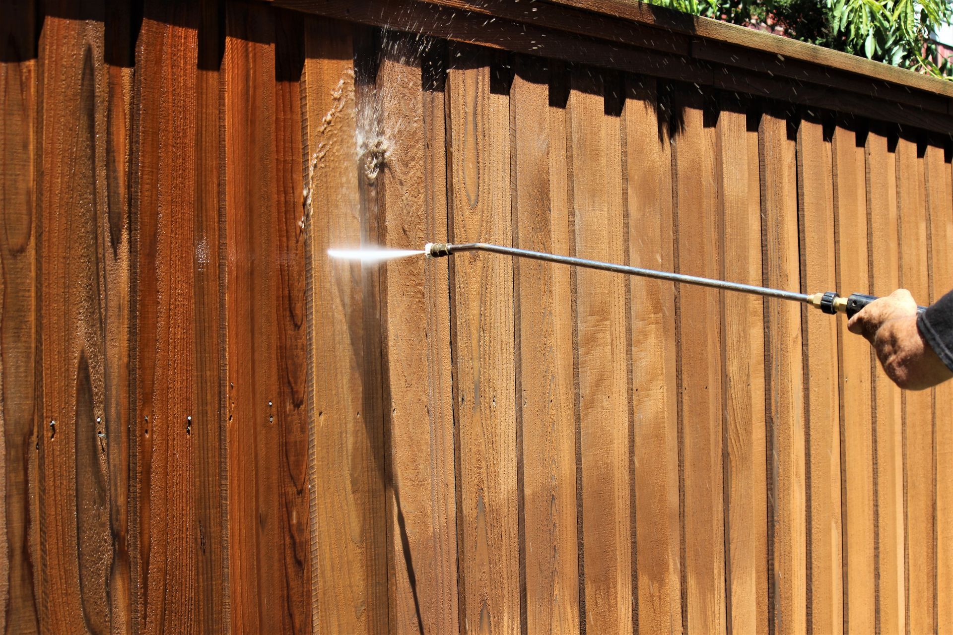 A person pressure washing a wooden fence, spraying water across the wood.