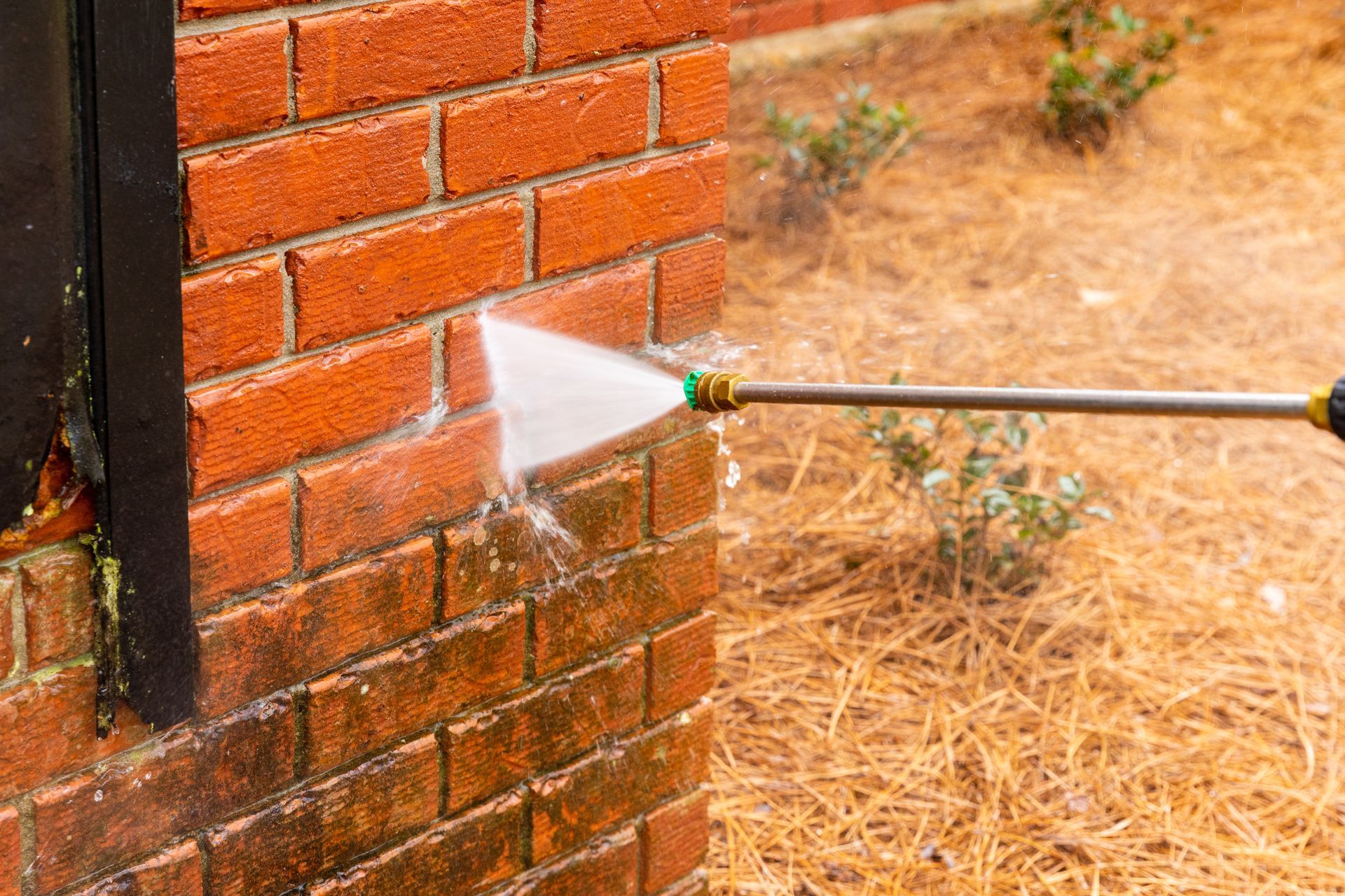 A person pressure washing a red brick wall to remove grime, outdoors.