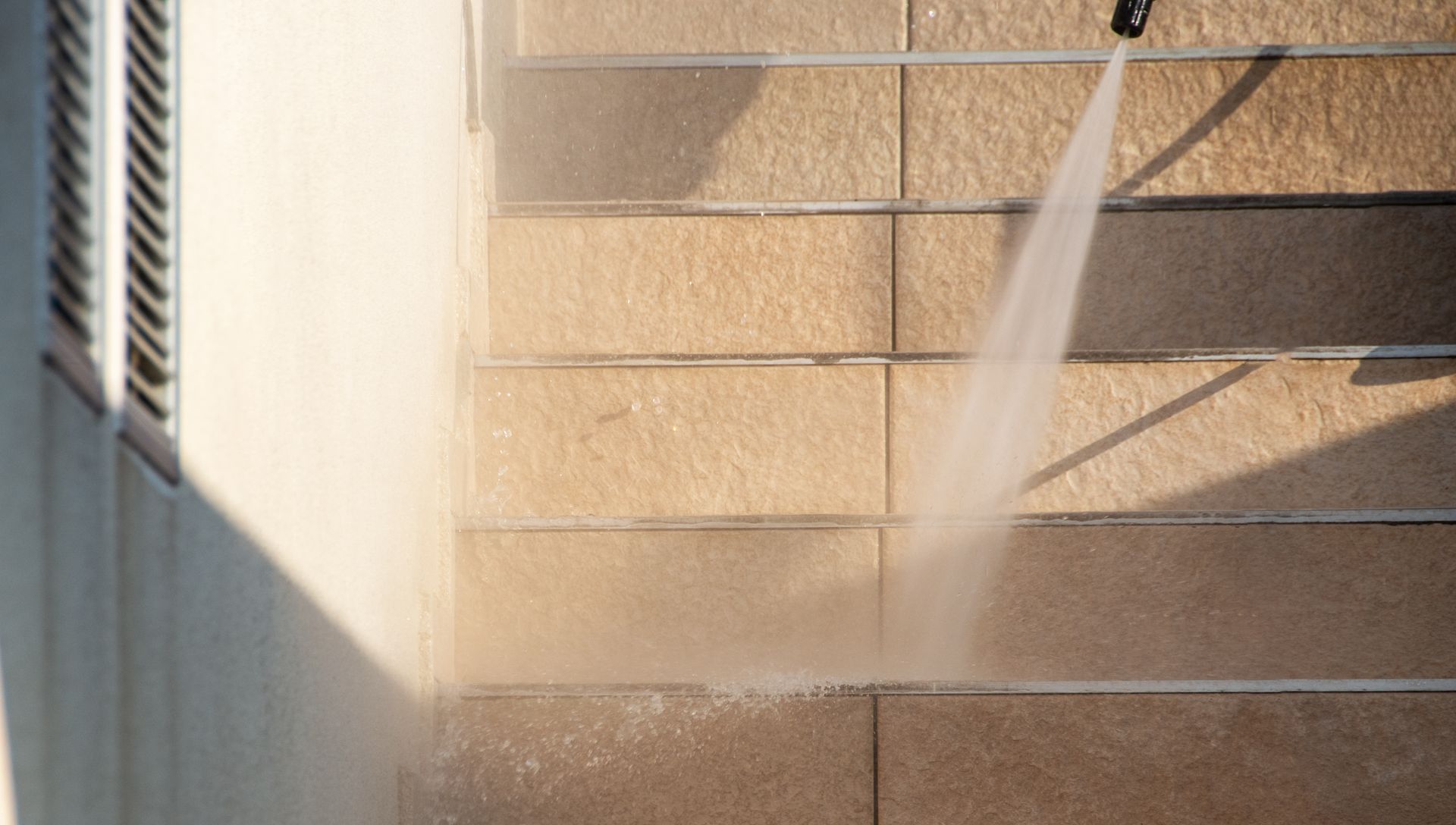 A pressure washer cleans a set of outdoor concrete stairs, spraying a stream of water across the steps.