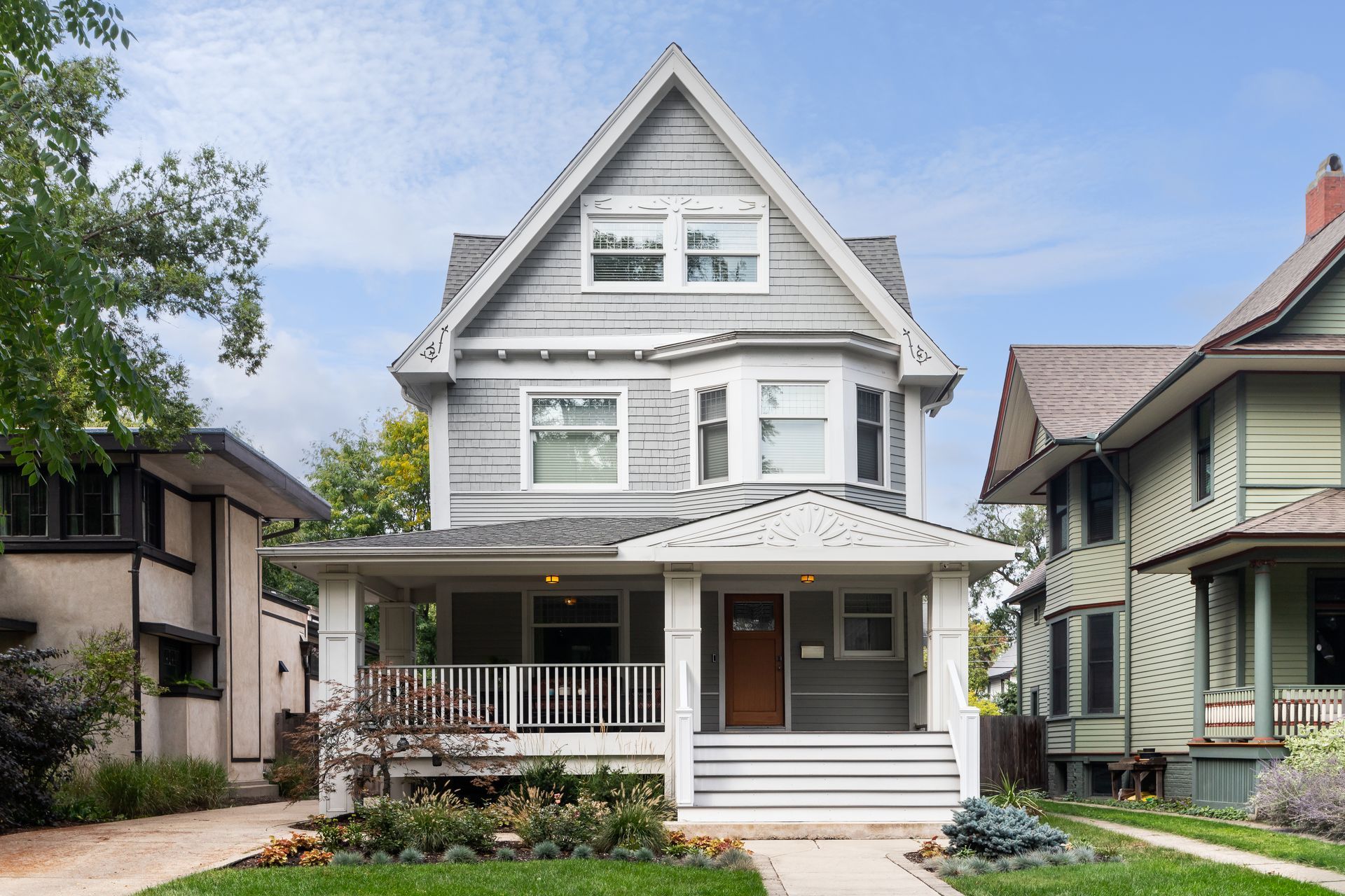 White two-story house with a front porch, gabled roof, and green lawn on a residential street