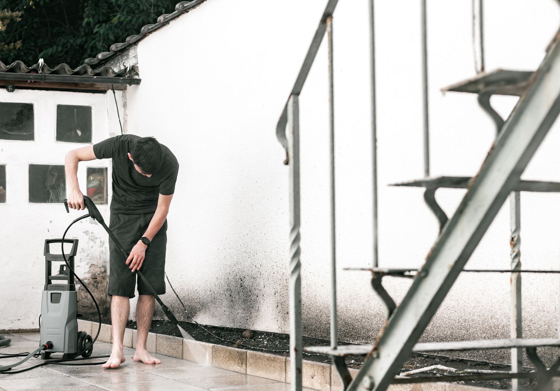 Person pressure washing a white wall outdoors near a building and metal staircase