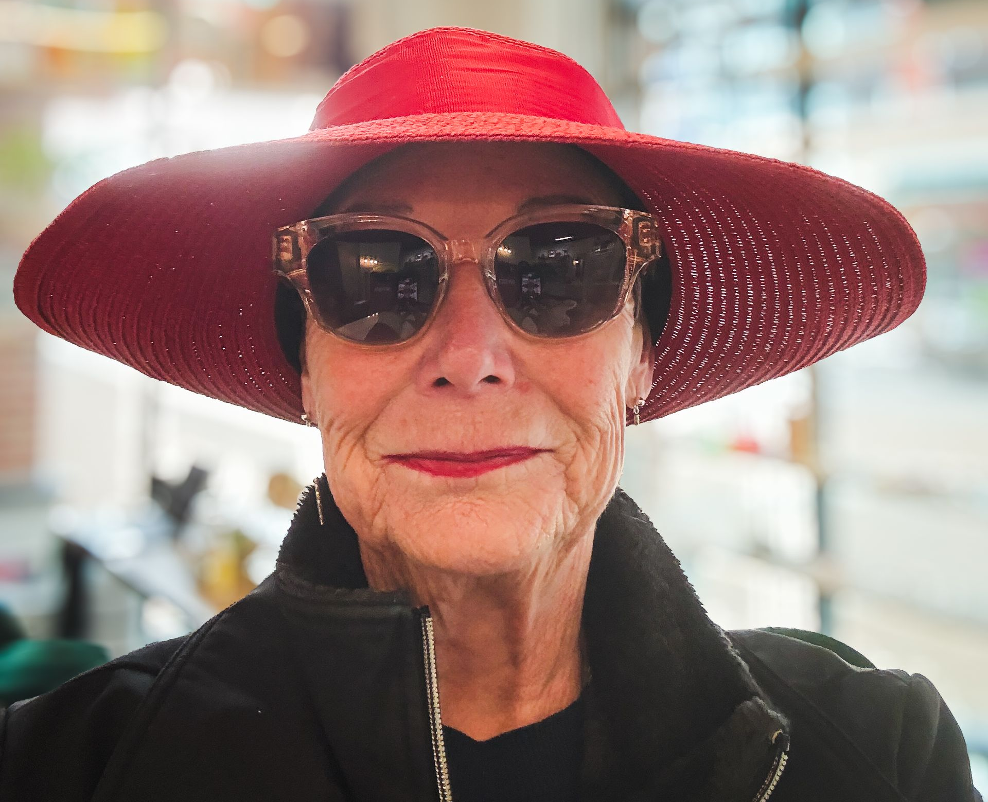Person wearing a wide red hat and sunglasses, standing outdoors with a faint smile.