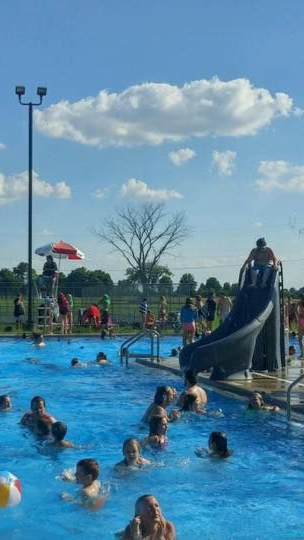 Outdoor pool with swimmers and a blue slide under a sunny sky