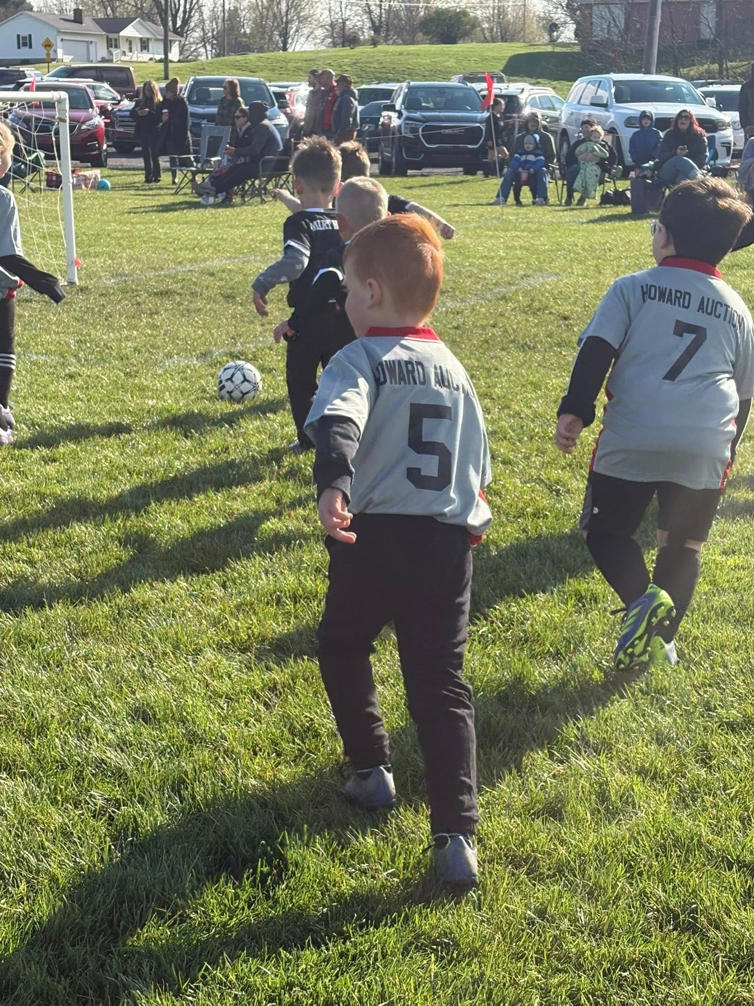 Children playing soccer on a grassy field, with players in white jerseys running toward the ball.