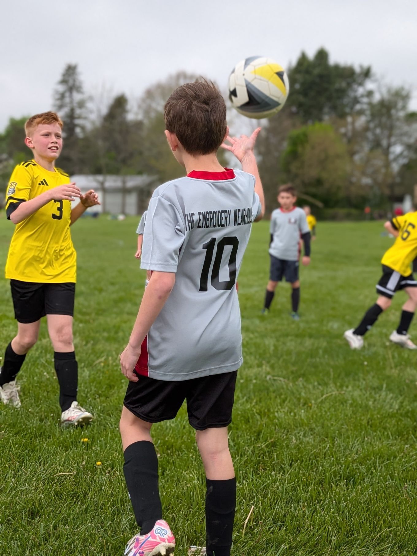 Children playing soccer on a grassy field, with one boy in a gray jersey heading the ball.