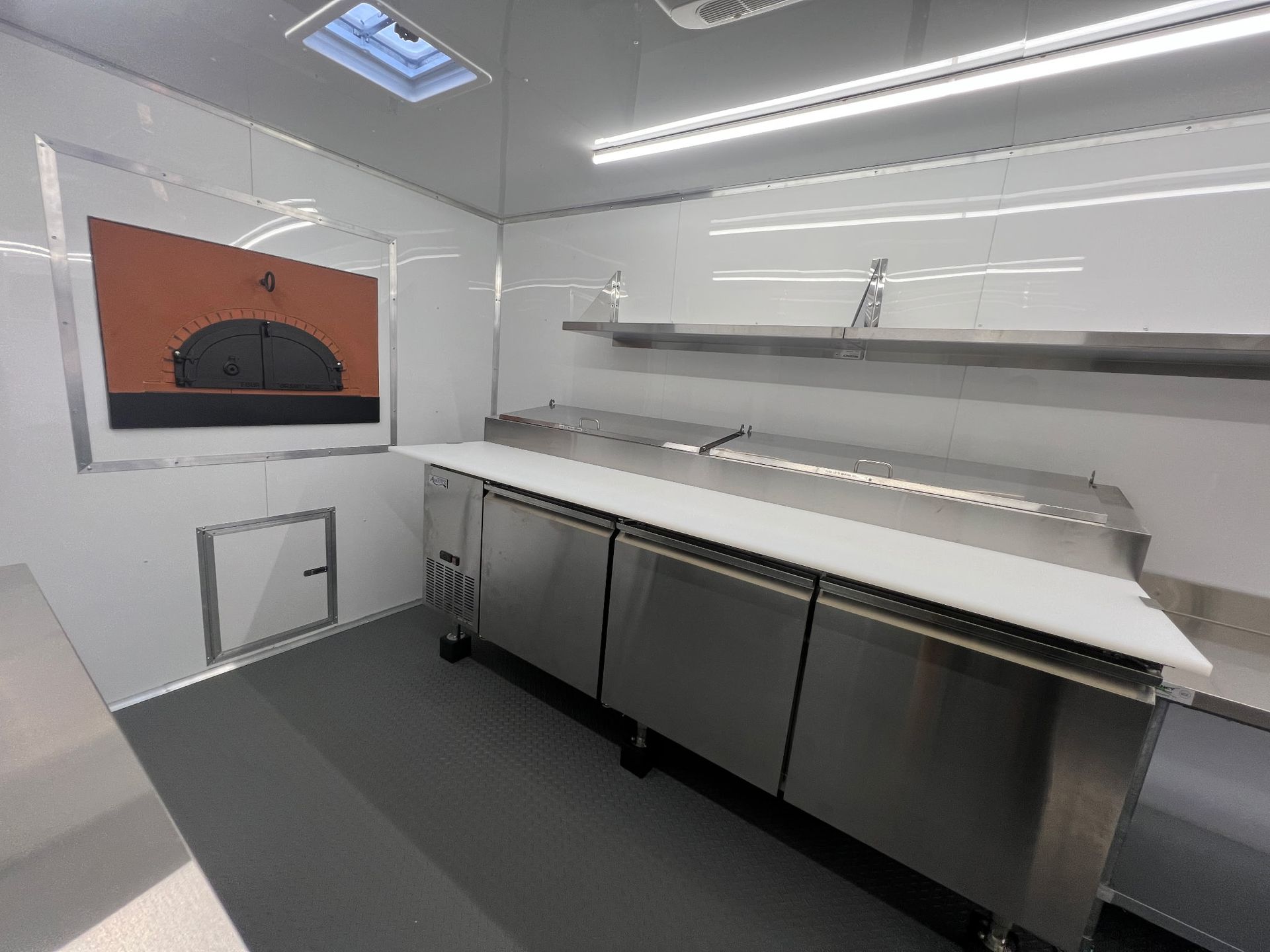 Empty commercial kitchen with stainless steel counters, white shelves, and orange wall art.