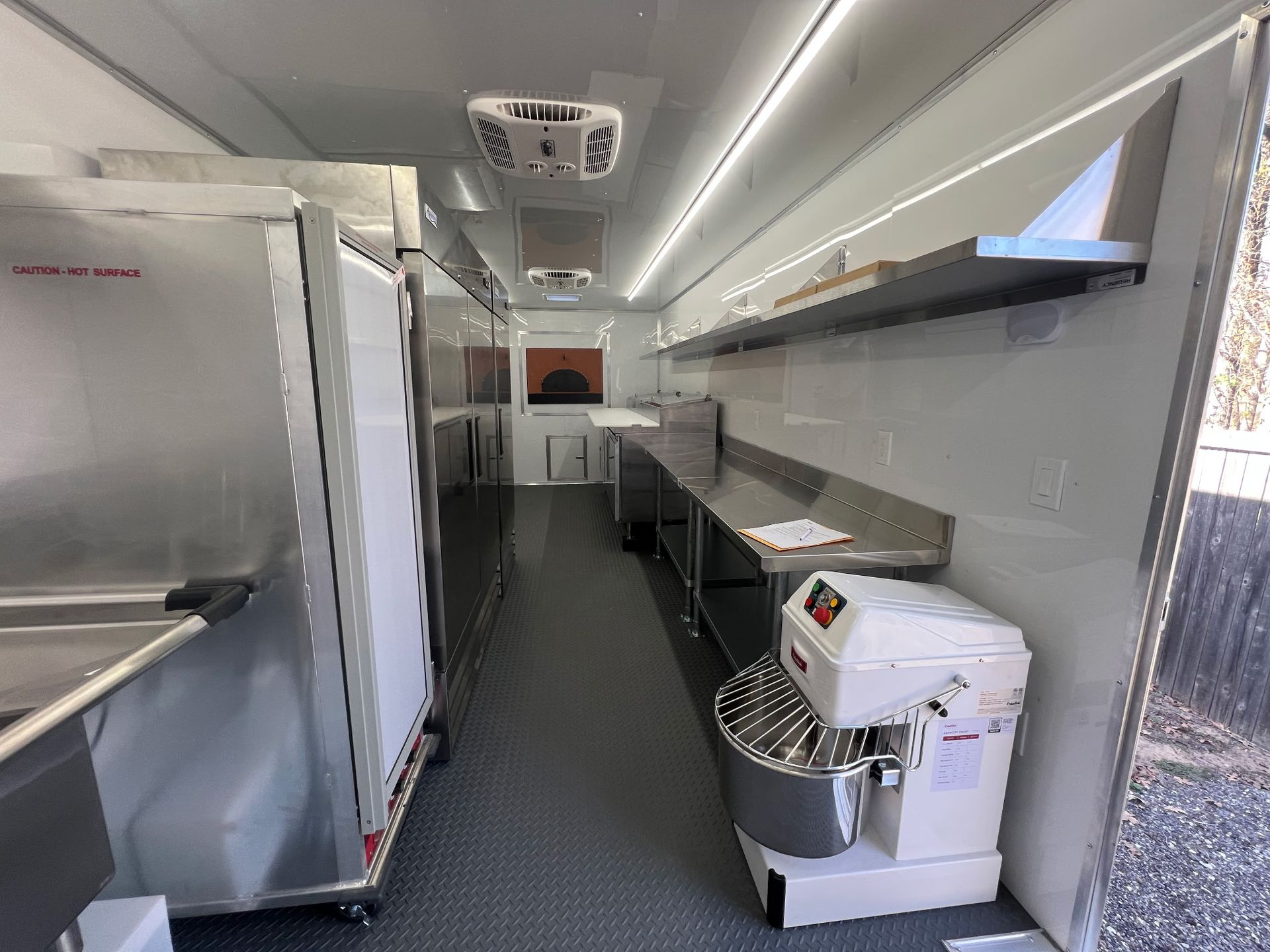 Mobile kitchen trailer with stainless steel counters, sink, and prep equipment inside a narrow work space