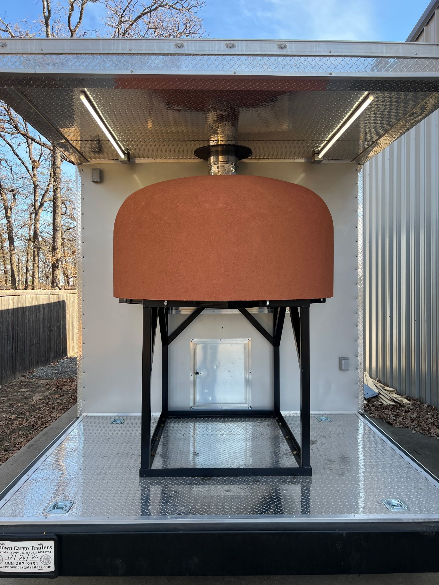 Outdoor insulated tank or vessel inside a metal shelter on a raised platform, in a wooded yard.