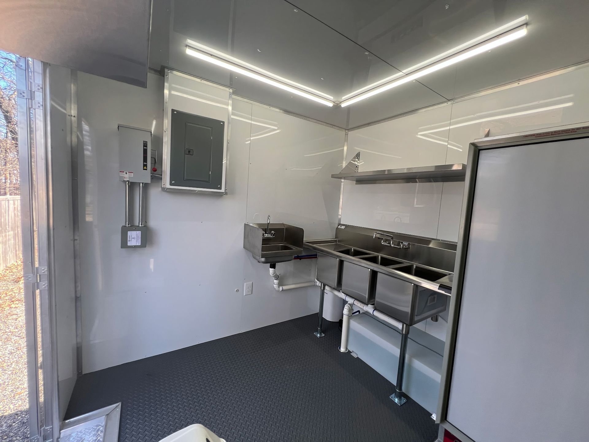 Small commercial kitchen with stainless steel counters, sink, and bright LED strip lighting.