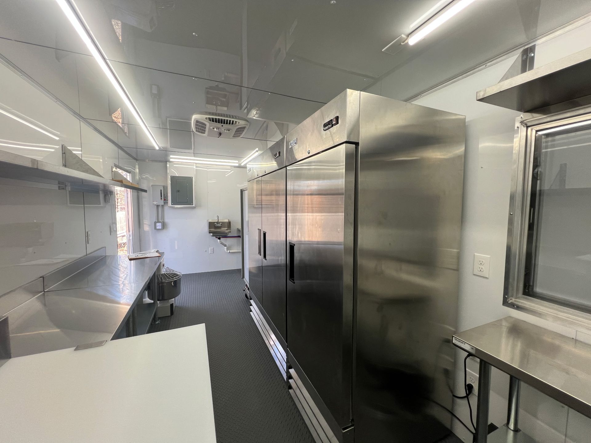Interior of a stainless-steel food truck with counters, shelves, and overhead lights