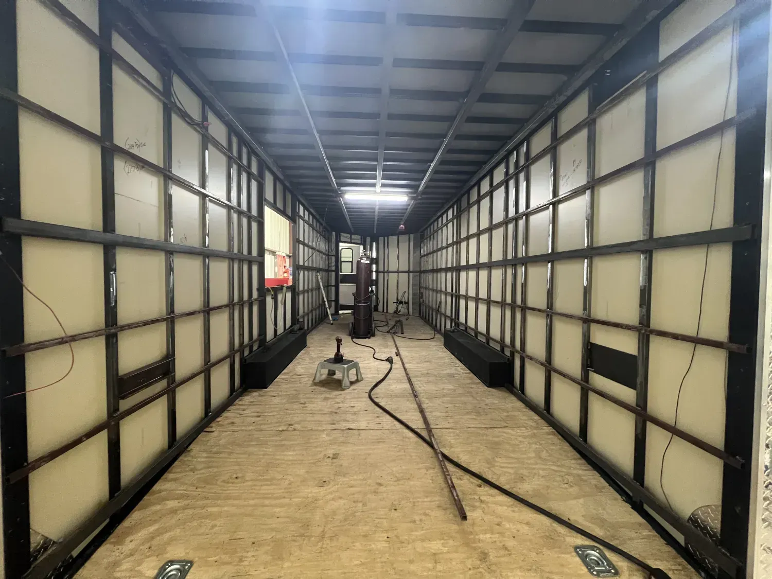 Inside a long industrial trailer unfinished metal walls, exposed ceiling, and floor tools with cables.