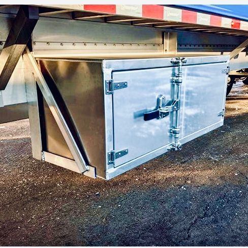 Metal trailer side with open silver cargo door and latch, parked on asphalt underneath a striped awning