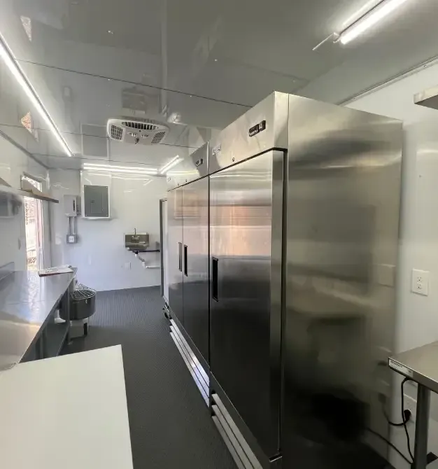 Bright commercial kitchen with stainless steel refrigerators and white counters under fluorescent lights