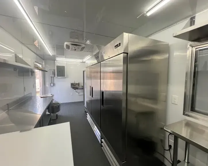 Sterile stainless-steel commercial kitchen corridor with refrigerators, counters, and bright overhead lights