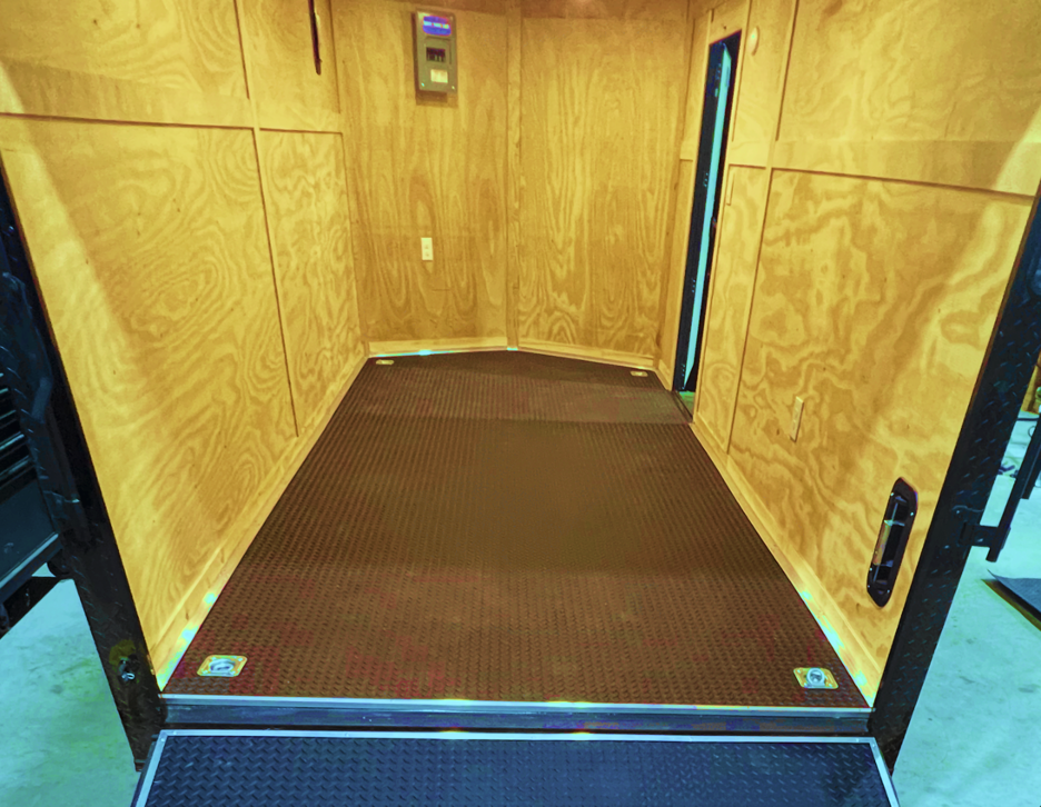 Wood-paneled cargo trailer  interior with a brown floor and open doorway