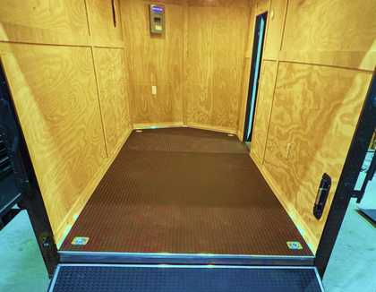Wood-paneled cargo trailer interior with a brown floor and open doorway