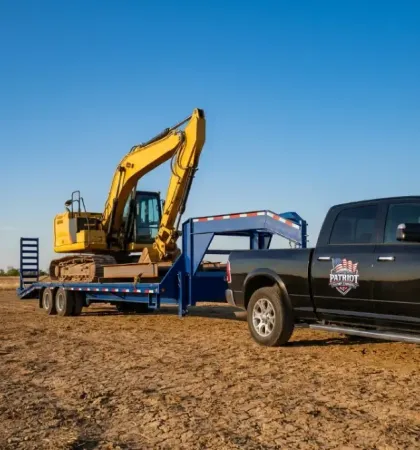 Black pickup truck towing a flatbed trailer with a yellow excavator on a dirt lot under a blue sky