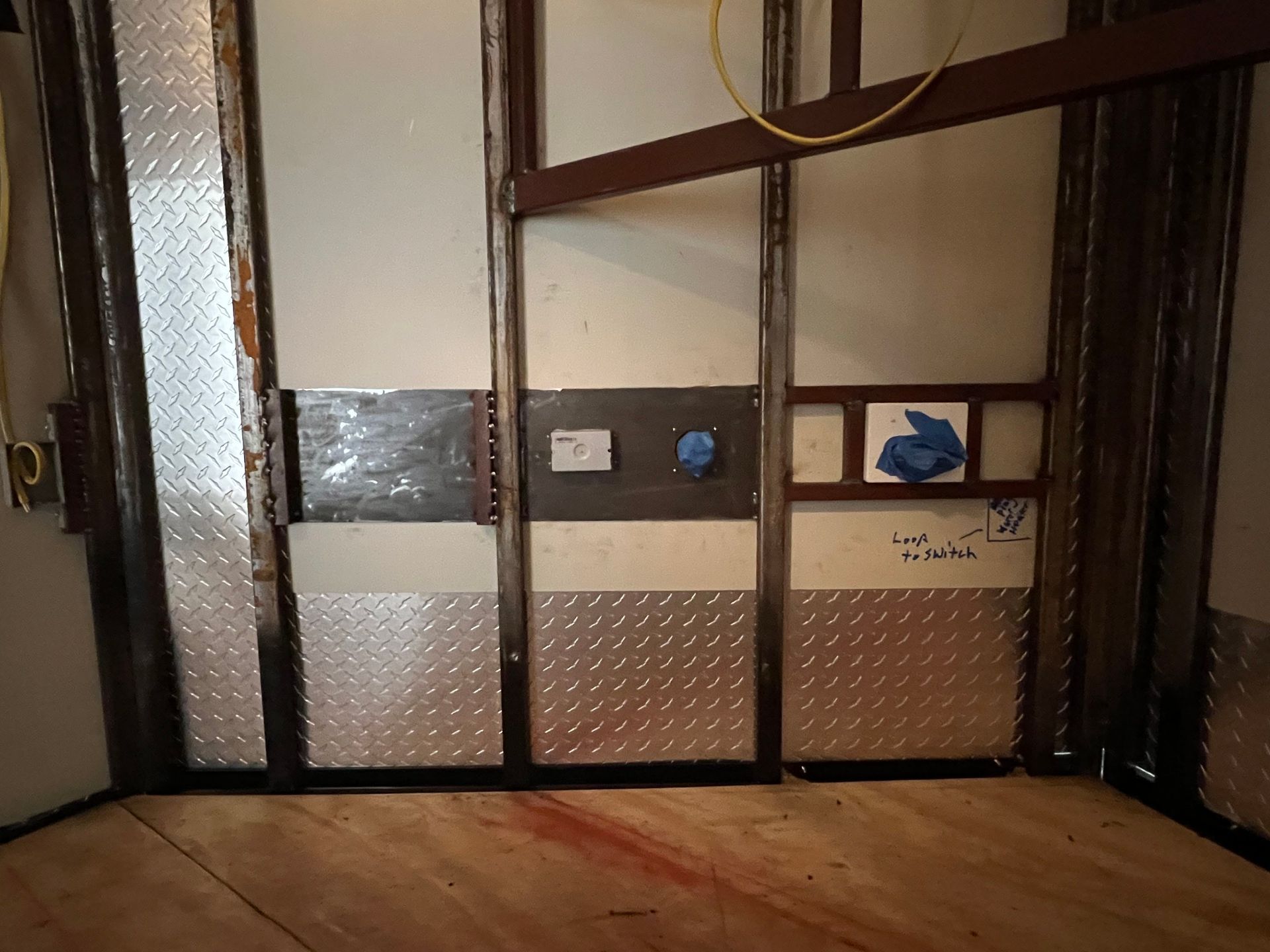 Empty room with metal walls, frosted door, and a small panel with outlets and blue tape.