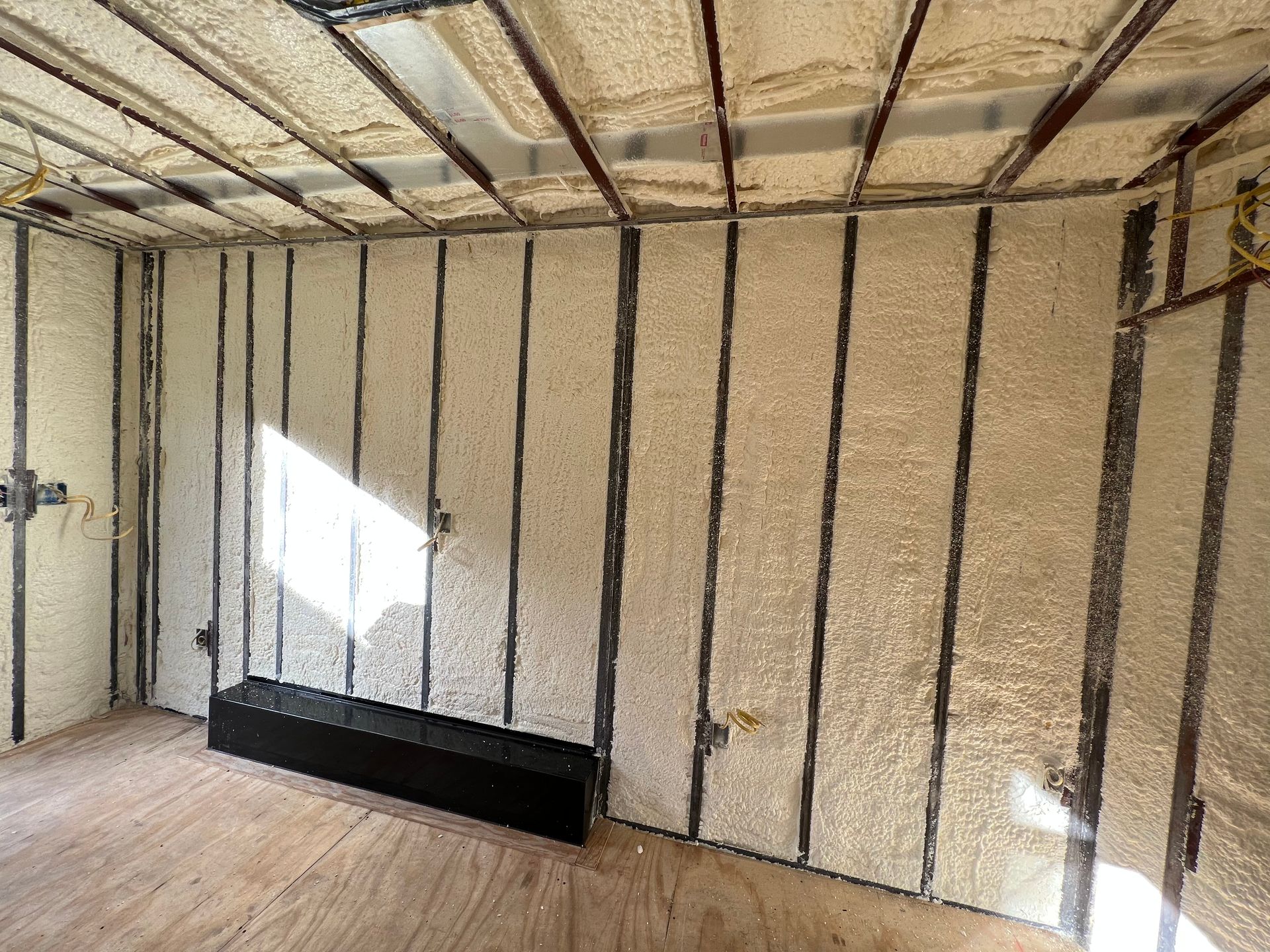 Interior of an unfinished room with exposed framing, insulation, and a small black bench by the wall.