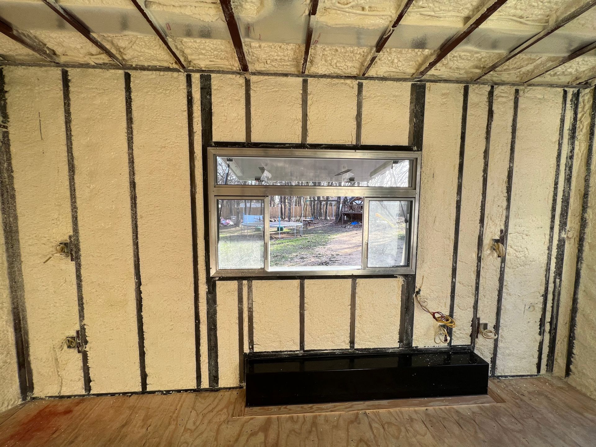 Interior wall framed with exposed studs, a small window, and a black bench below it.