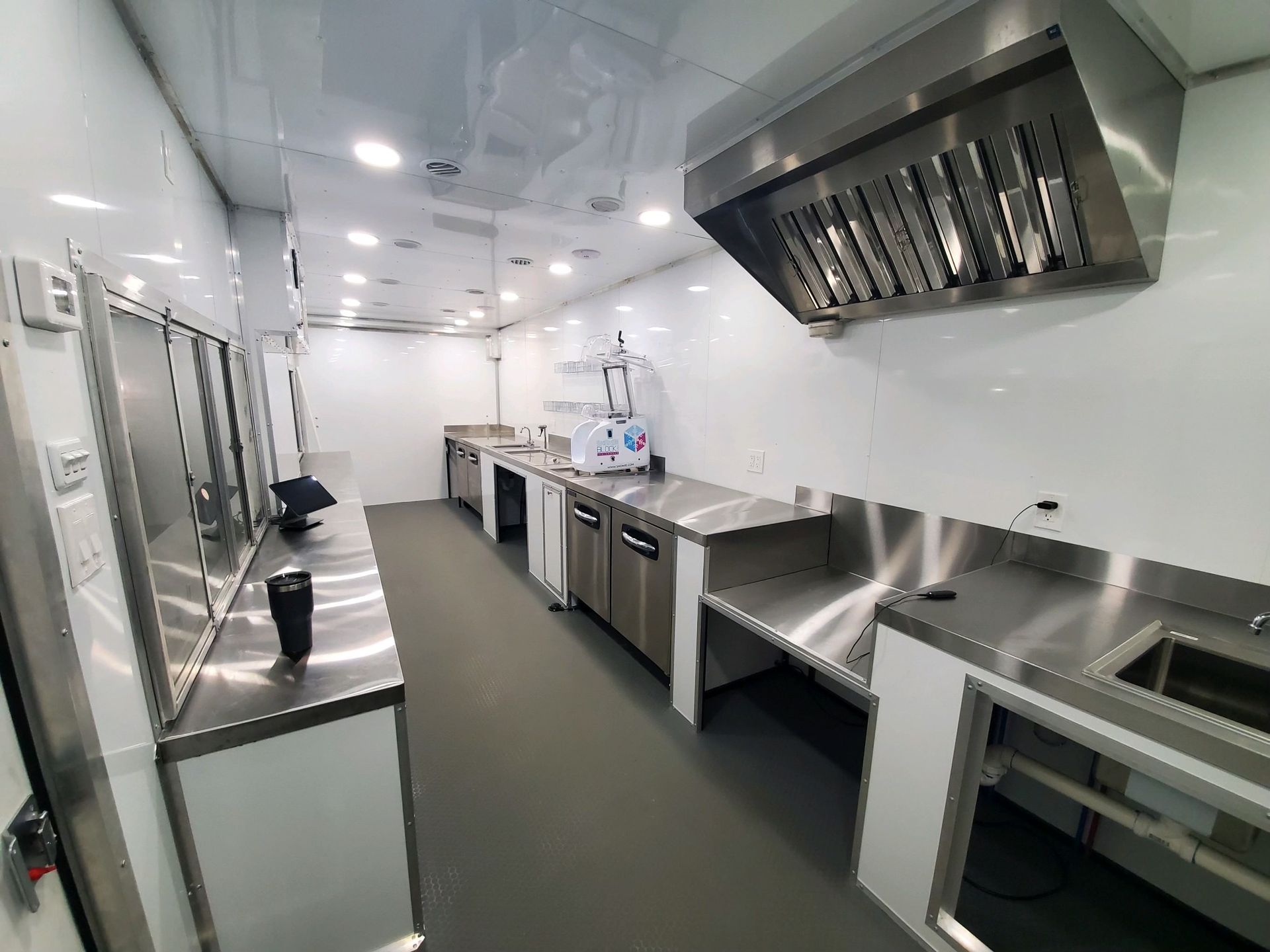 Modern stainless-steel commercial kitchen with counters, sinks, and overhead ventilation in a modern cargo trailer interior,