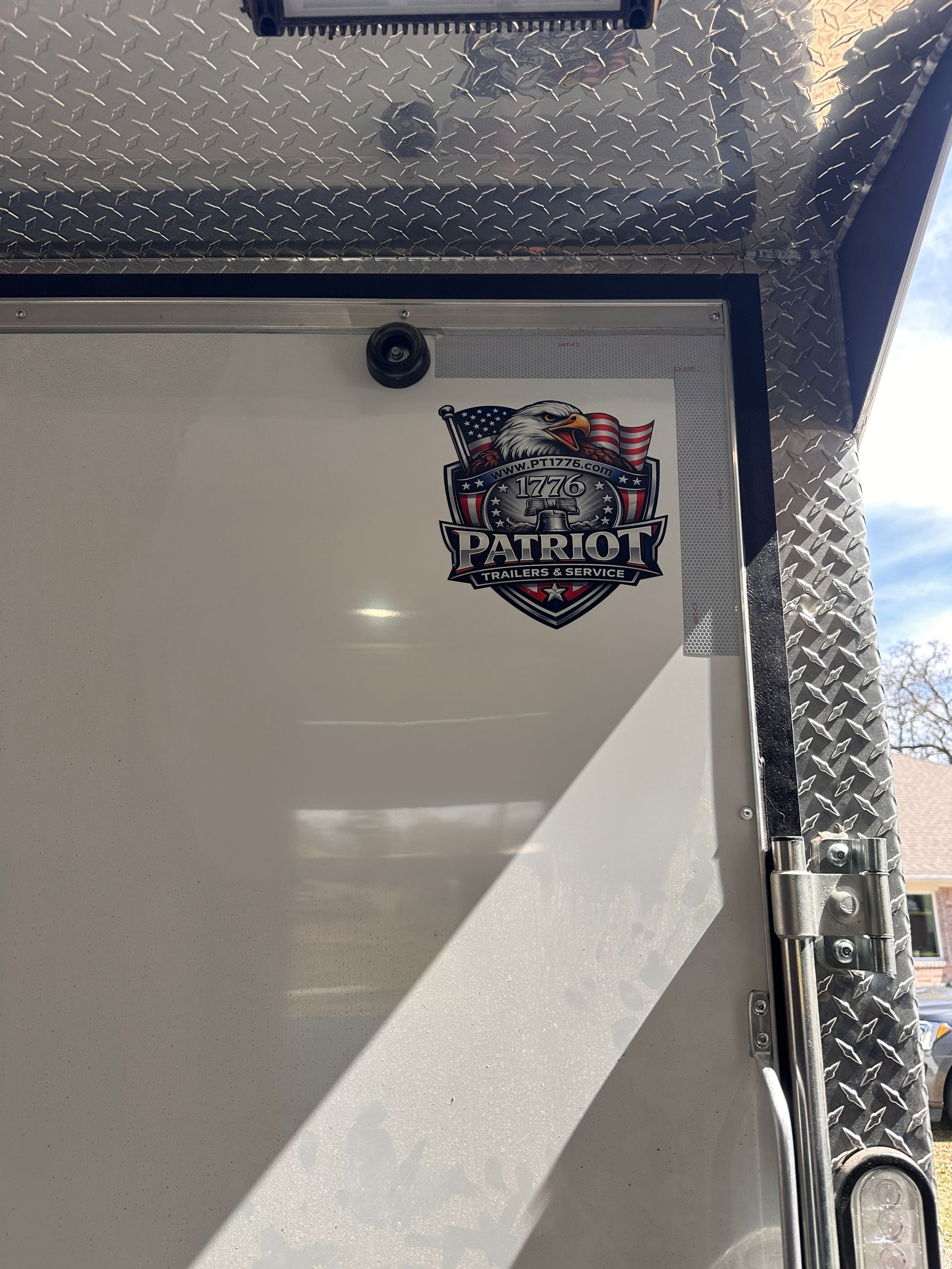 White camper door with a Patriots logo sticker and a black latch, framed by diamond-plate trim.