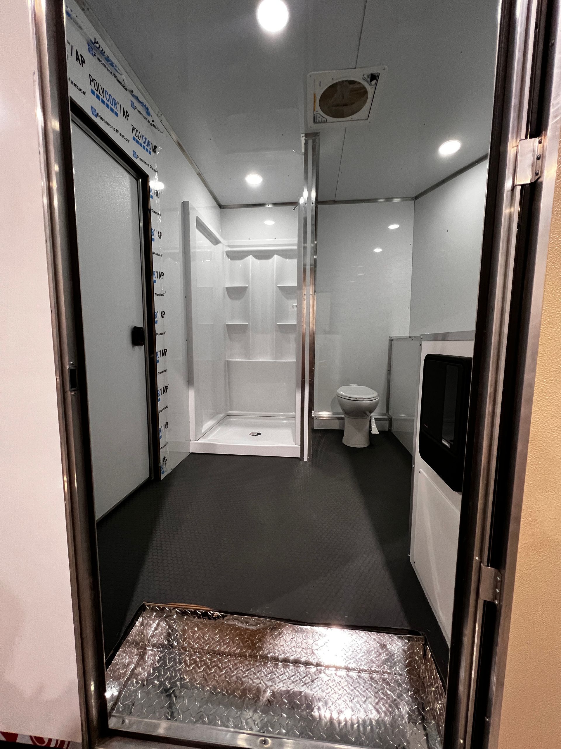 Interior of a small bathroom with a toilet, shower stall, sink, and black floor mats.
