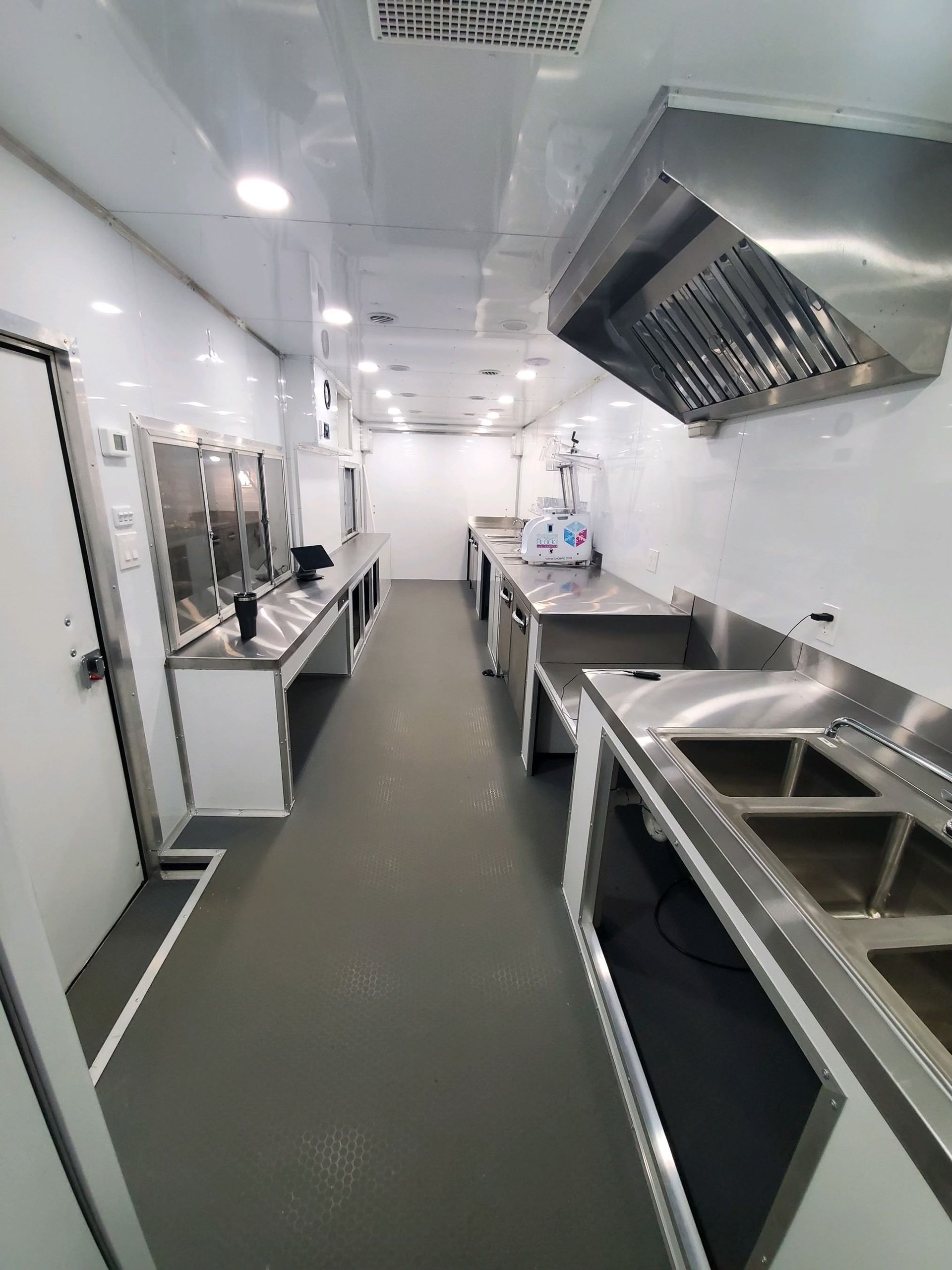 Sterile commercial kitchen with stainless steel counters, sinks, and ventilation in a narrow white corridor