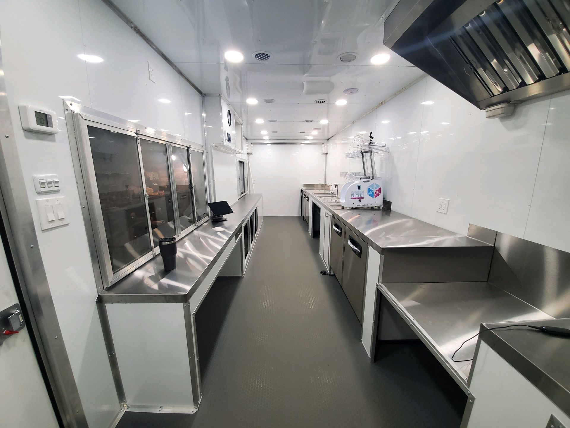 Inside a mobile kitchen trailer ,empty stainless-steel commercial kitchen with counters, sinks, and exhaust hood