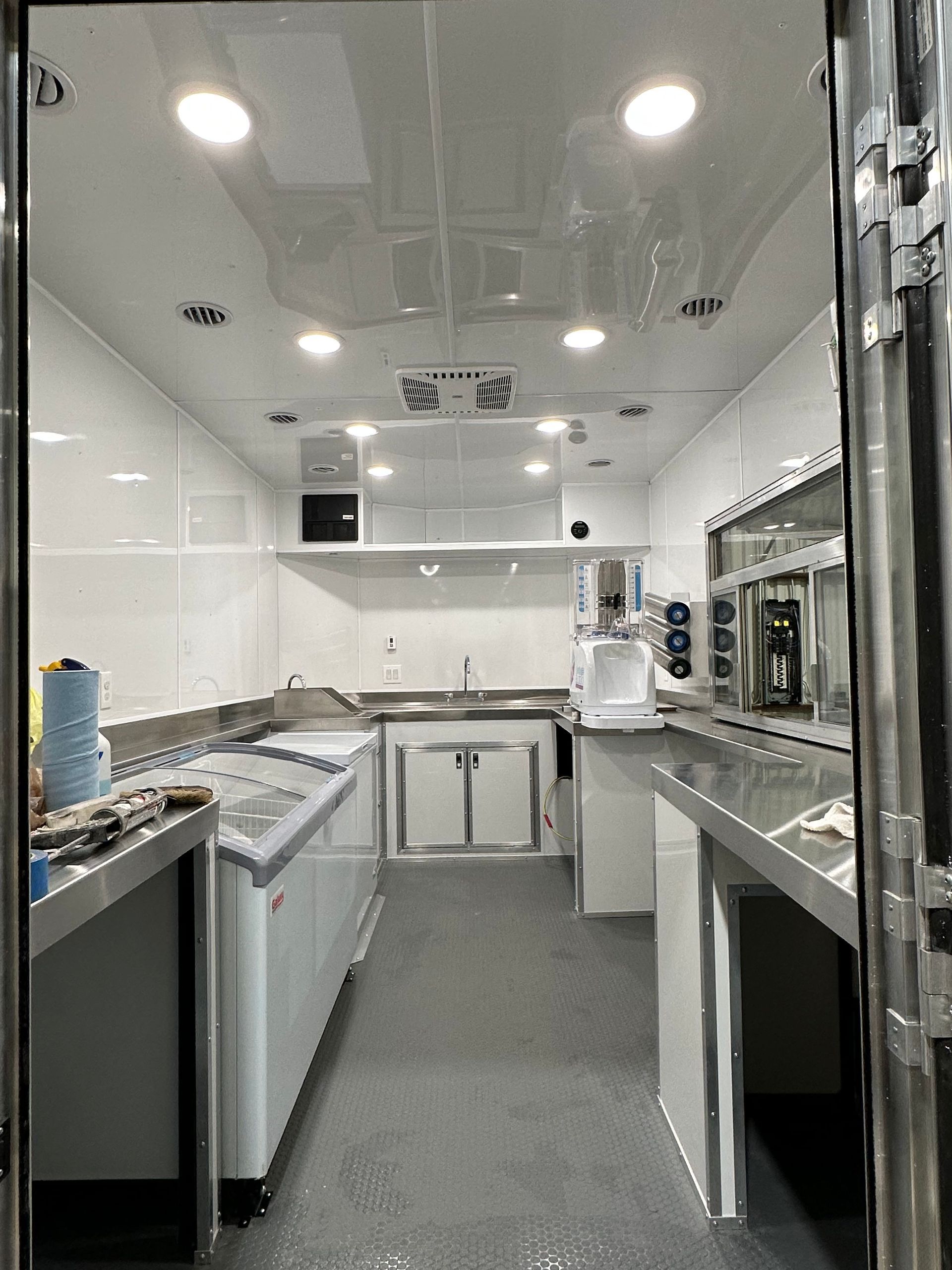 Narrow commercial kitchen with stainless steel counters, white cabinets, and bright overhead lights