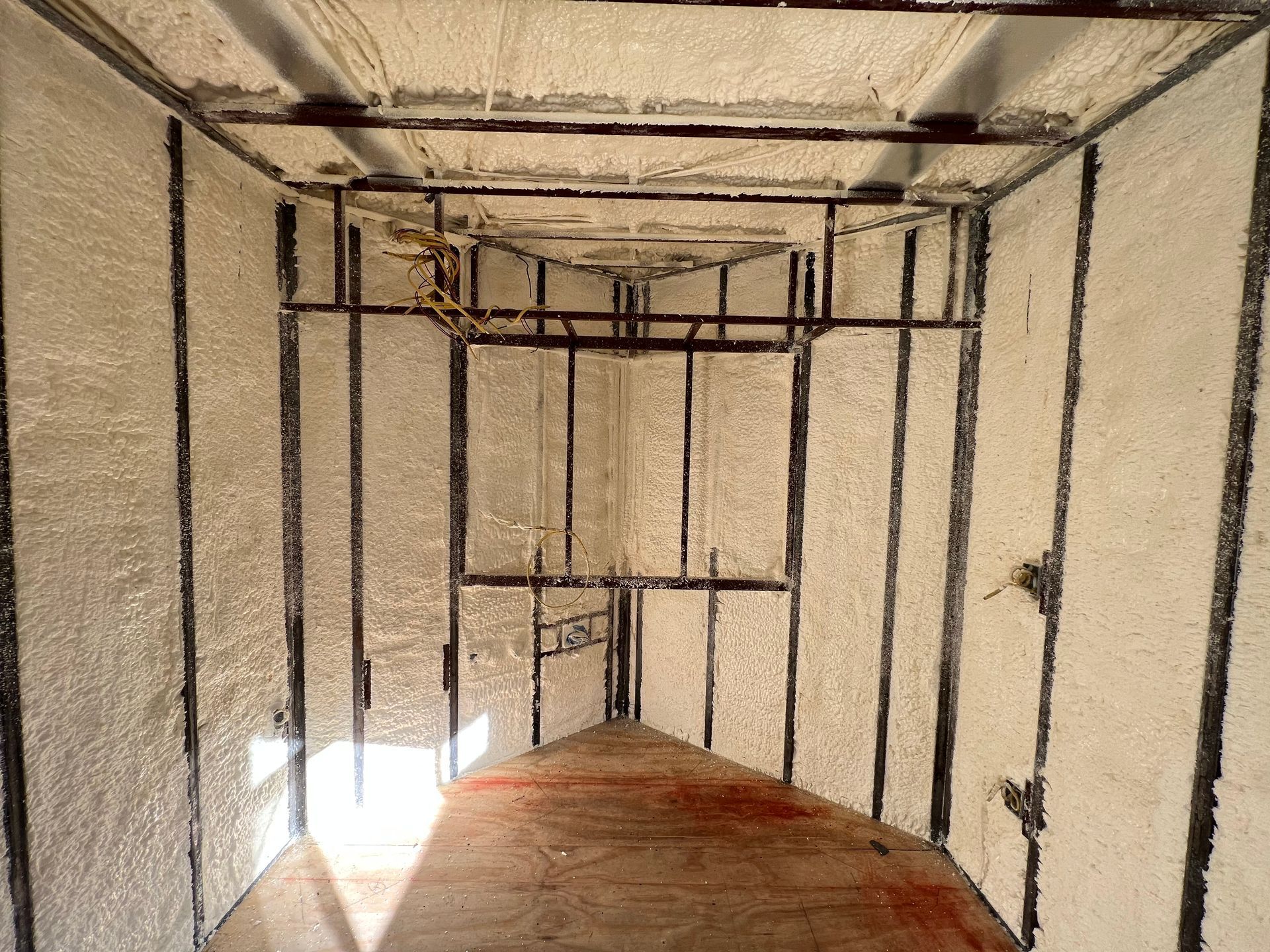 Narrow unfinished room with exposed framing, beige walls, and a reddish floor under construction.