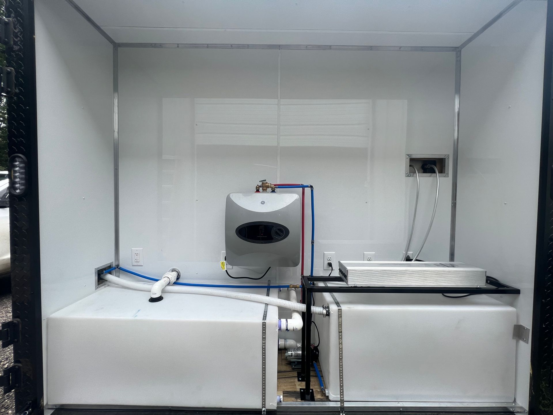 Interior of upgraded trailer with white tanks and a small gray device connected by blue and red tubing