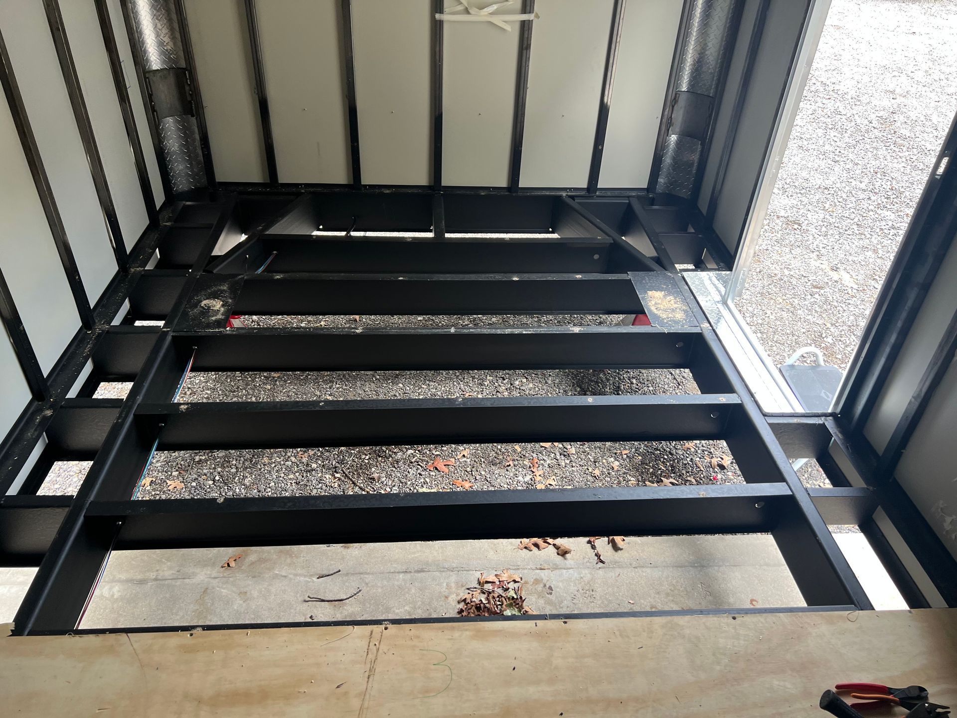 Frame of cargo trailer and wall panels during upgrade showing gravel below through the opening