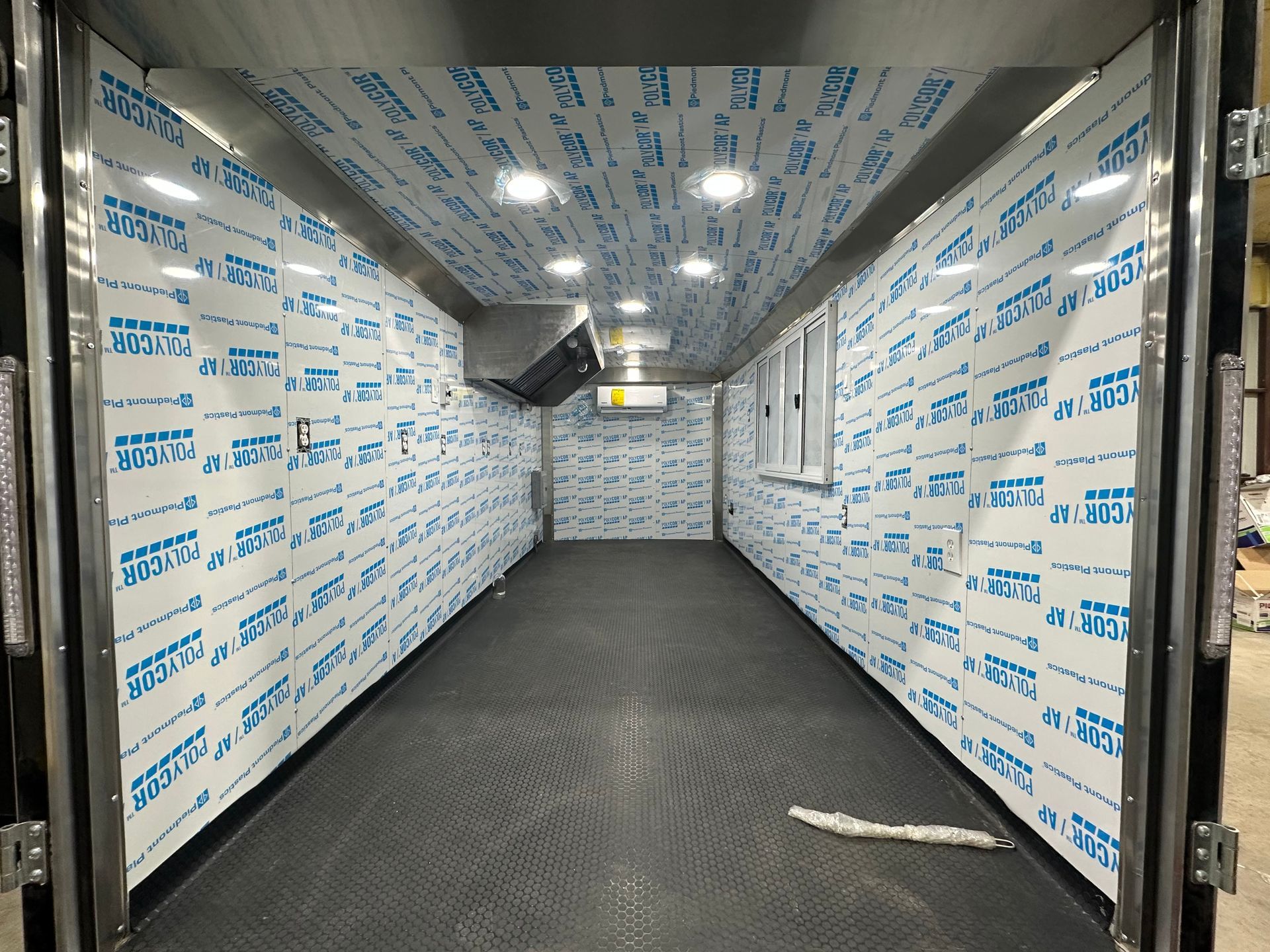Empty insulated cargo trailer interior with white protective walls and dark floor mats