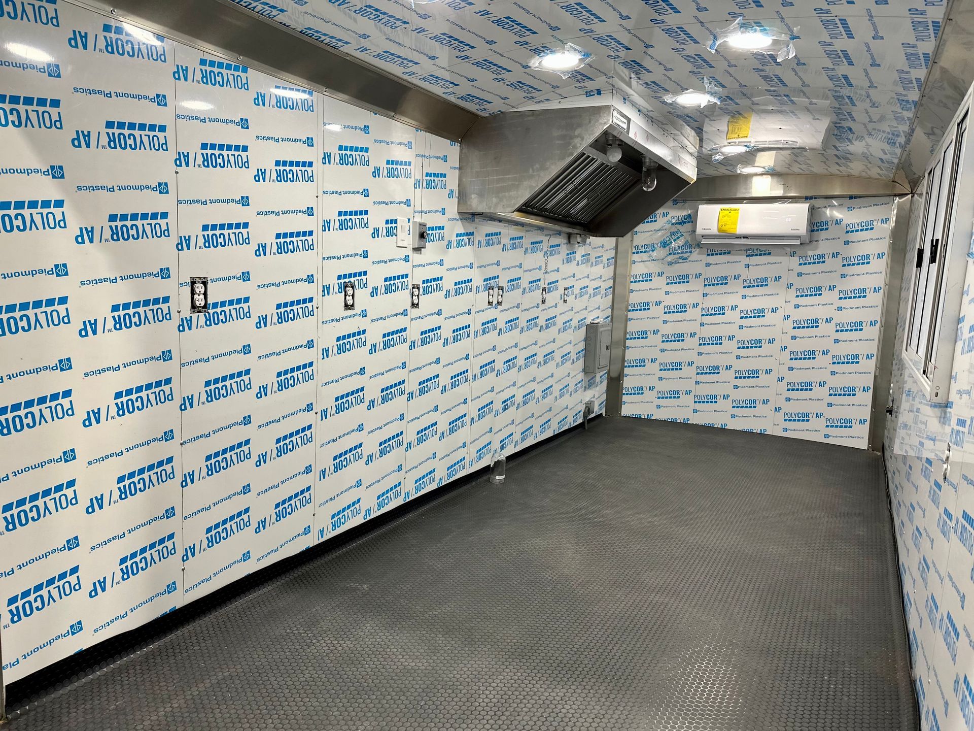 Empty insulated cargo trailer with white protective wall panels, gray floor, and ceiling-mounted black fixture.