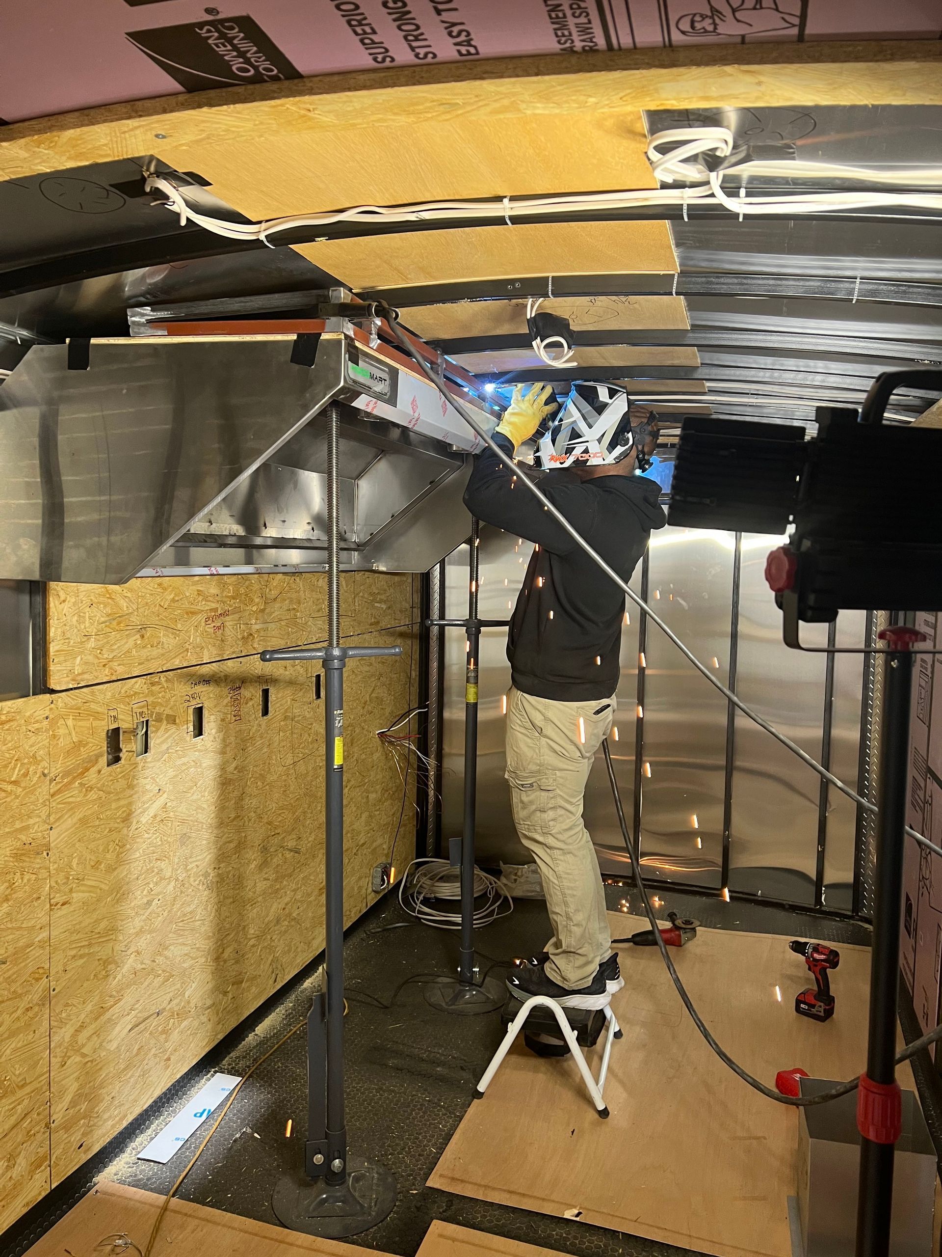 Patriot Trailers employee working overhead in a trailer interior with exposed insulation and wiring.