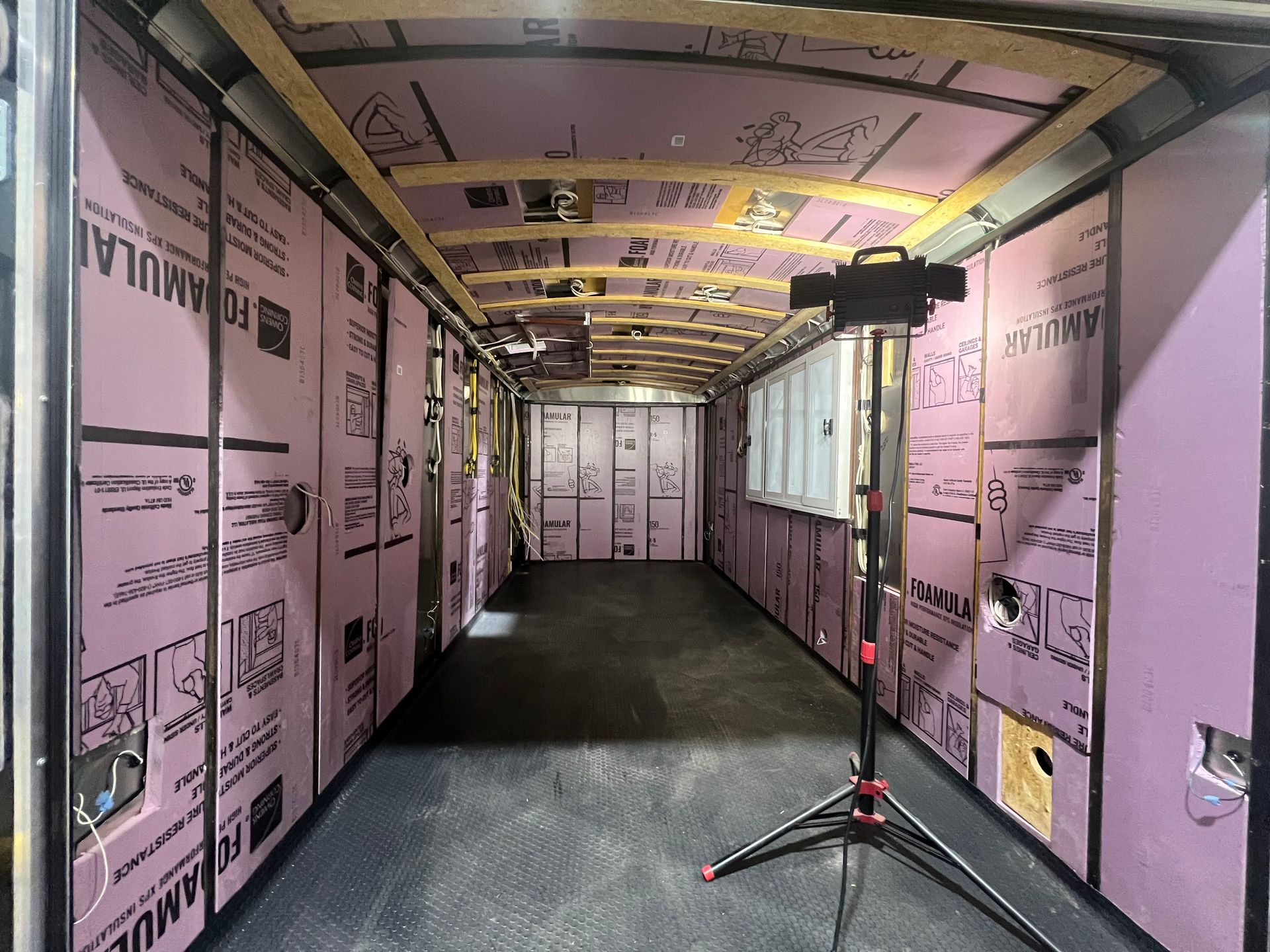 Insulated trailer interior with pink walls, black floor, and a tripod light stand near the back.
