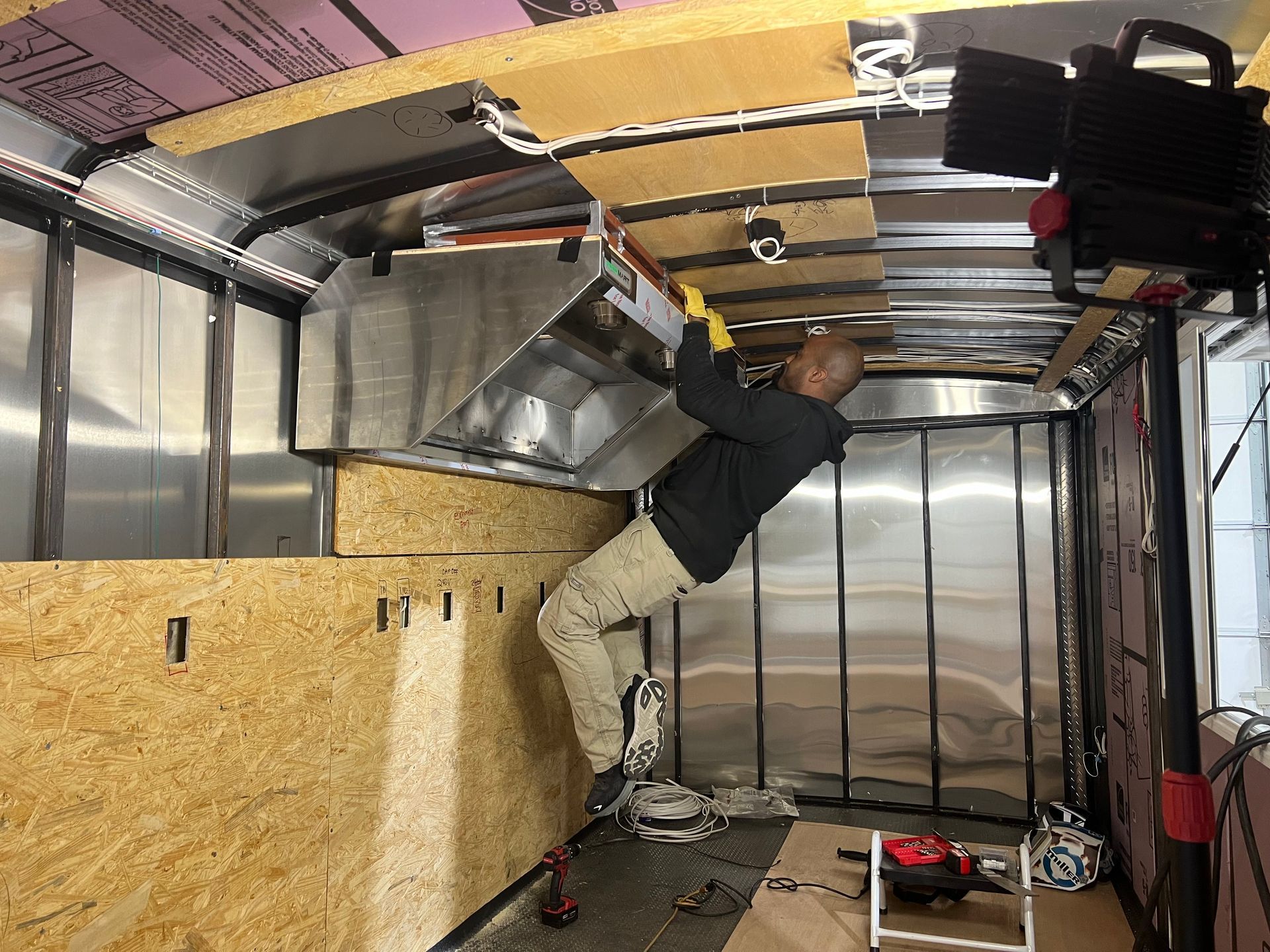 Patriot Trailers employee installing overhead wiring inside a van, leaning under the ceiling.