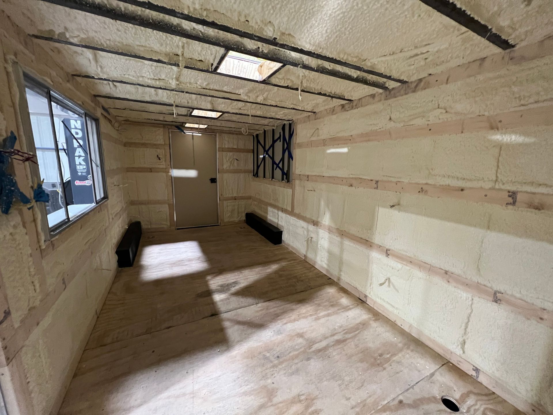 Empty trailer upgraded with bare insulation, window, and wood floor light from the left