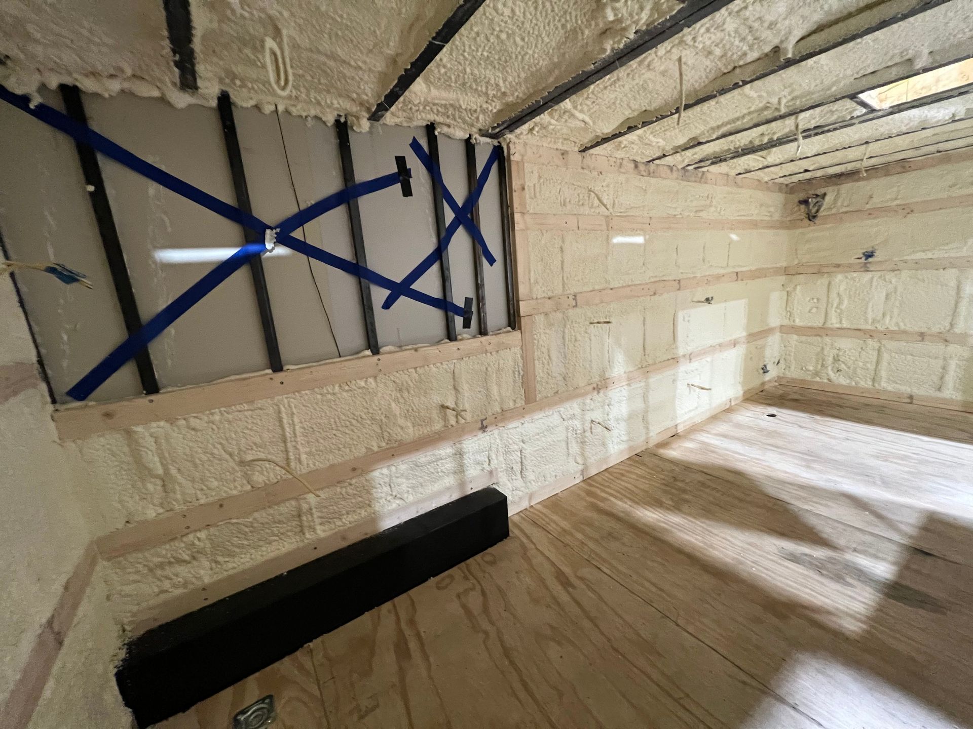 Empty trailer upgraded with tiled walls, wood floor, and blue tape on a wall opening.