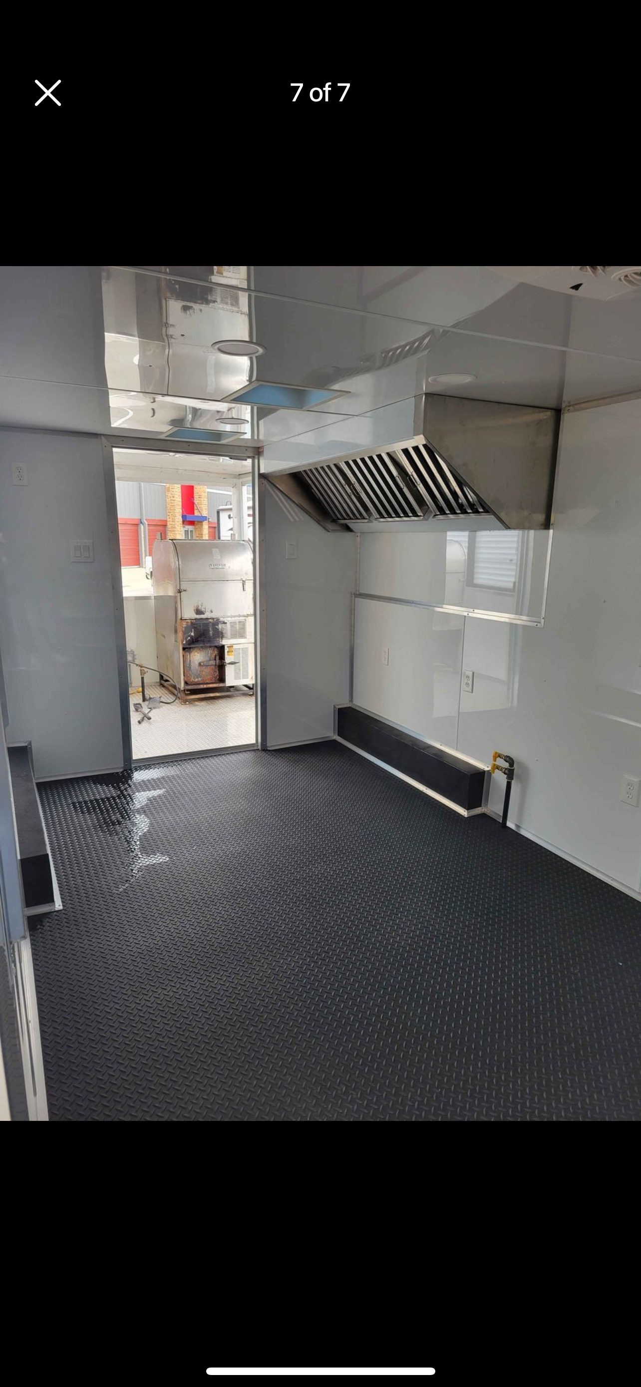 Empty industrial kitchen with stainless steel hood, white walls, and black diamond-plate floor.