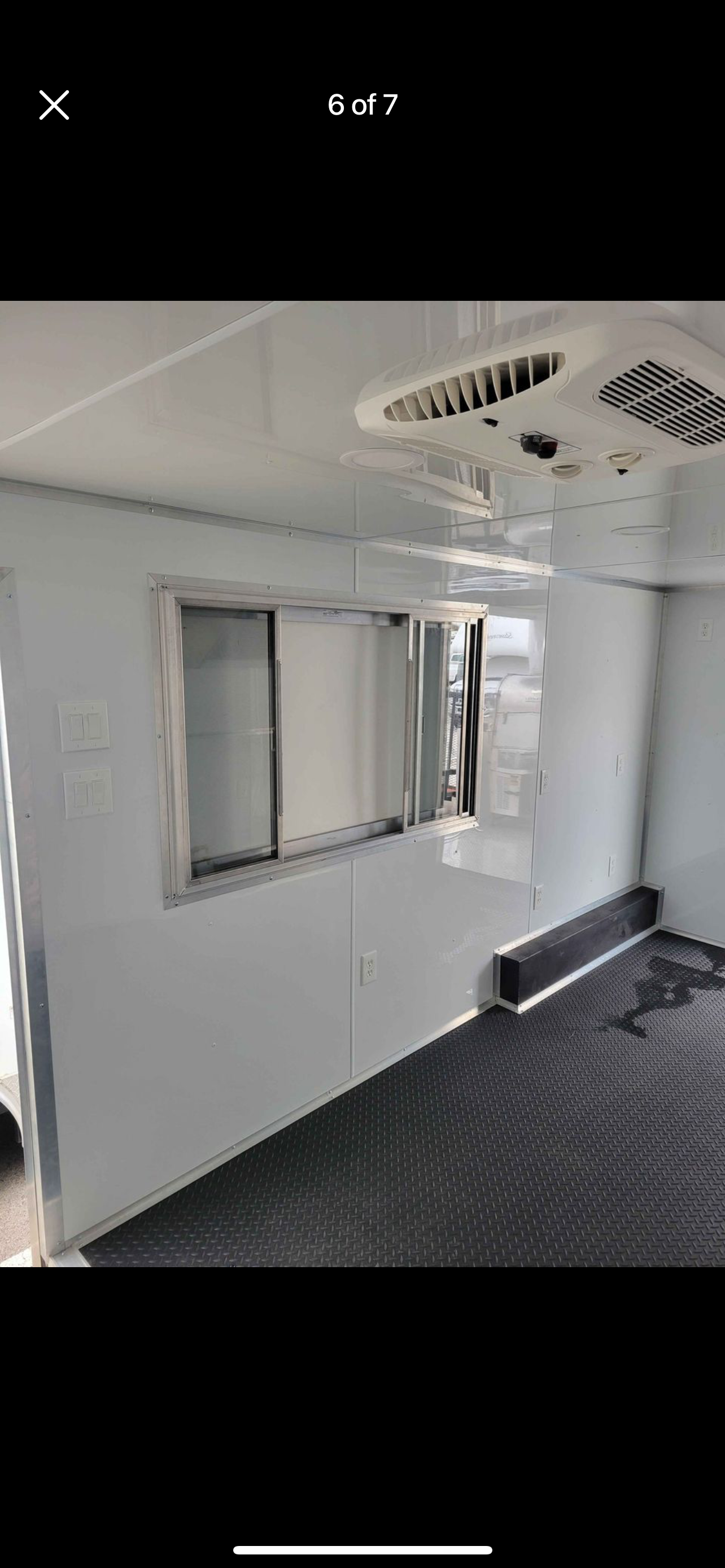 Empty white interior room with a window and patterned dark floor, likely inside a trailer or container