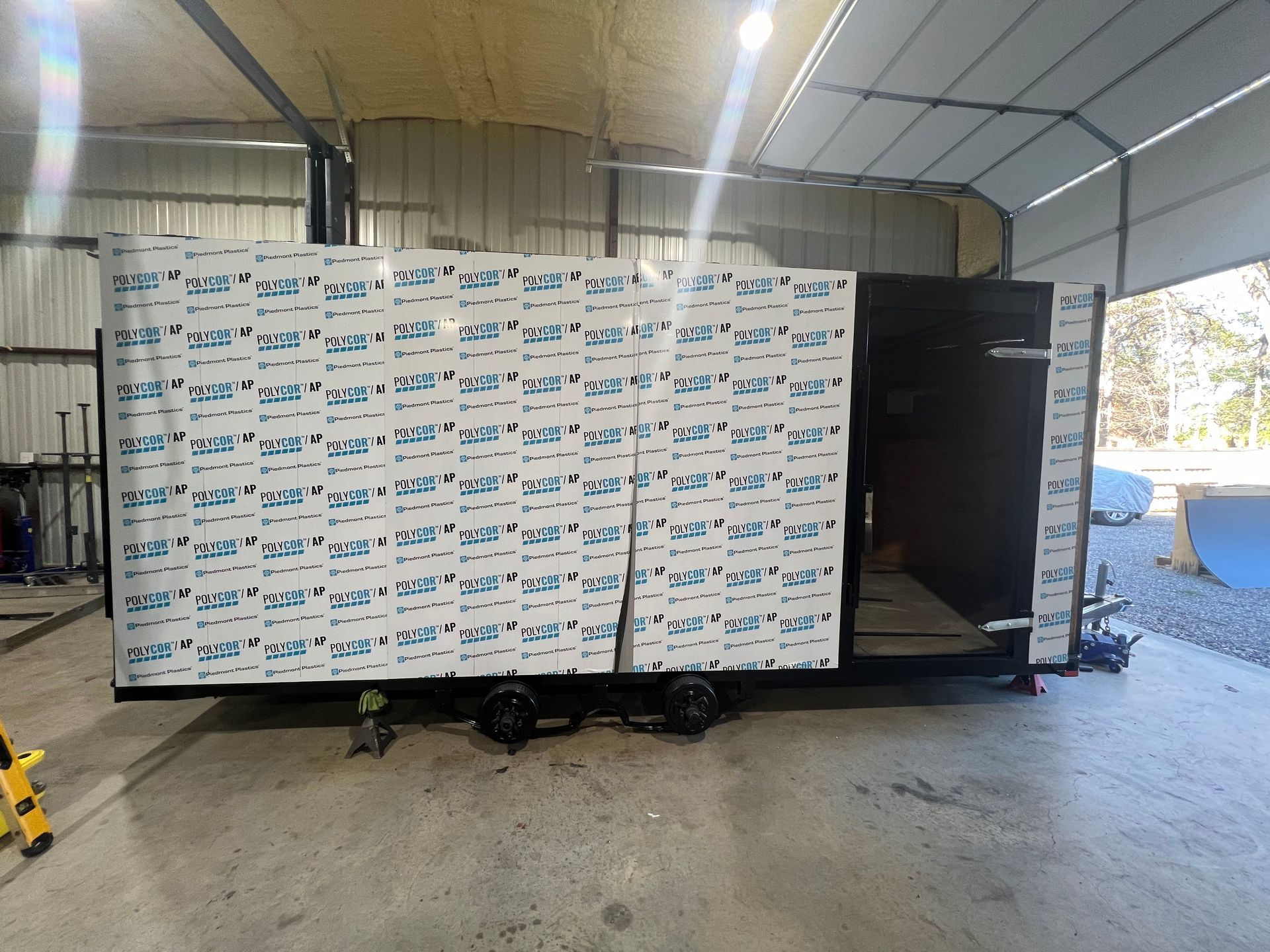 Insulated trailer with a large white-and-blue panel wall open in a warehouse-like workshop