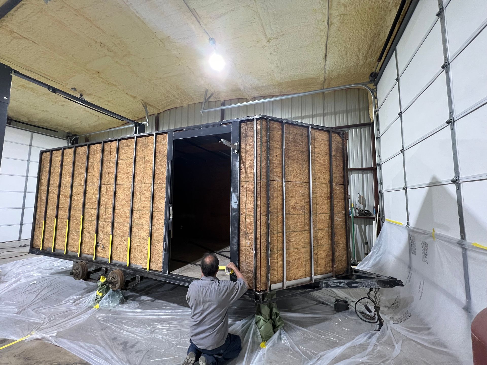 Insulated metal large brown cargo trailer in a warehouse, with a worker crouching near an open door.