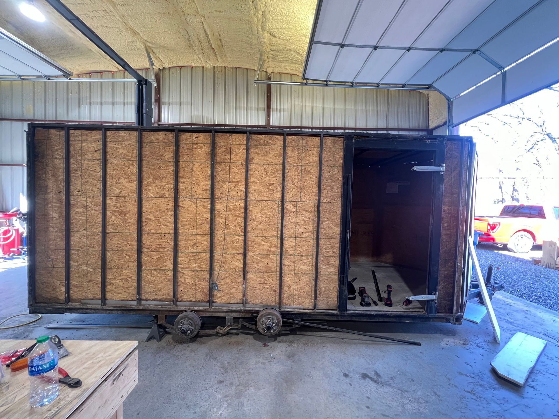 Large flatbed trailer with tan side panels parked under a roof in an open workshop area.